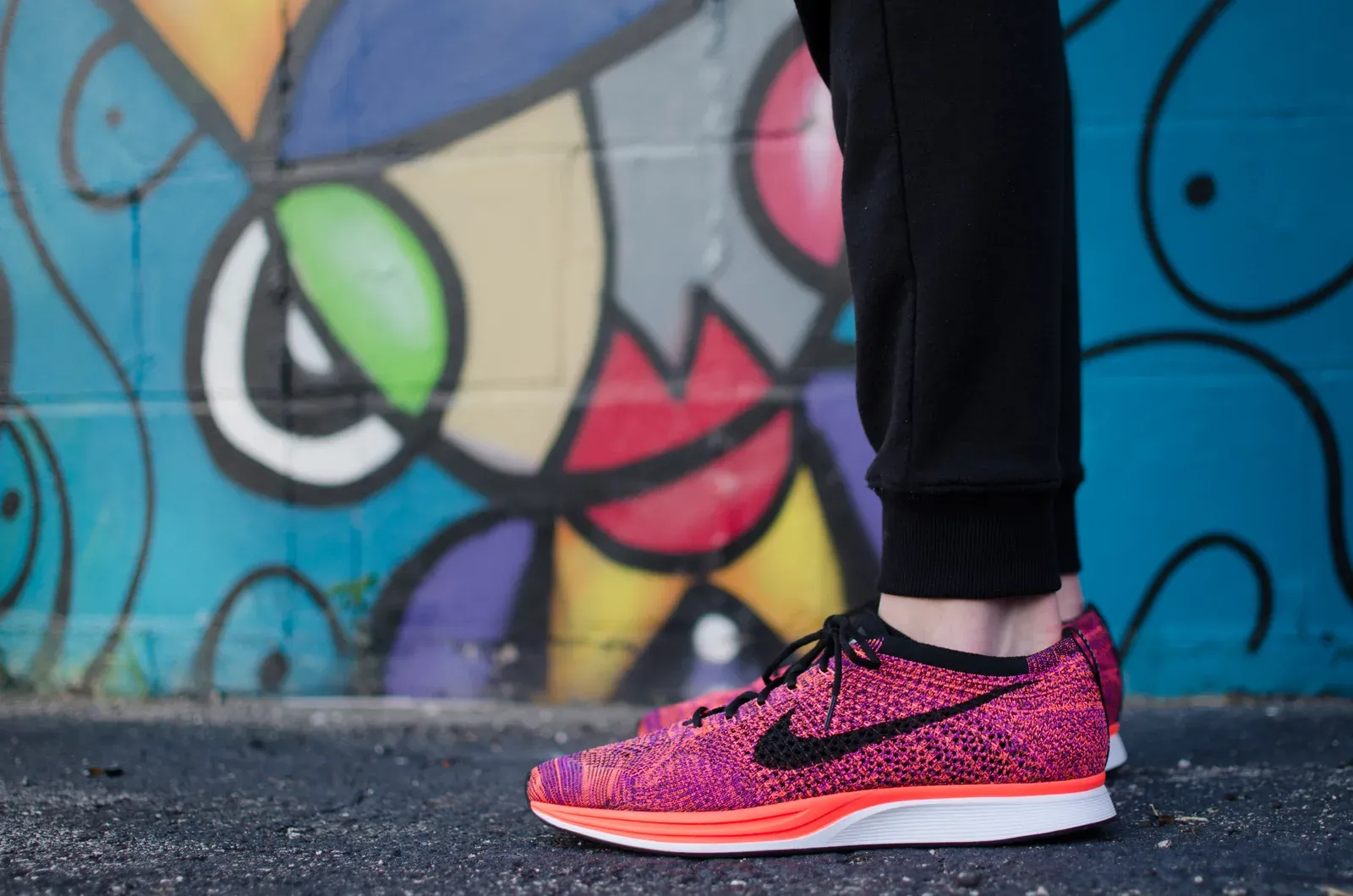 Chaussures de sport roses portées sur le bitume, devant un mur coloré.