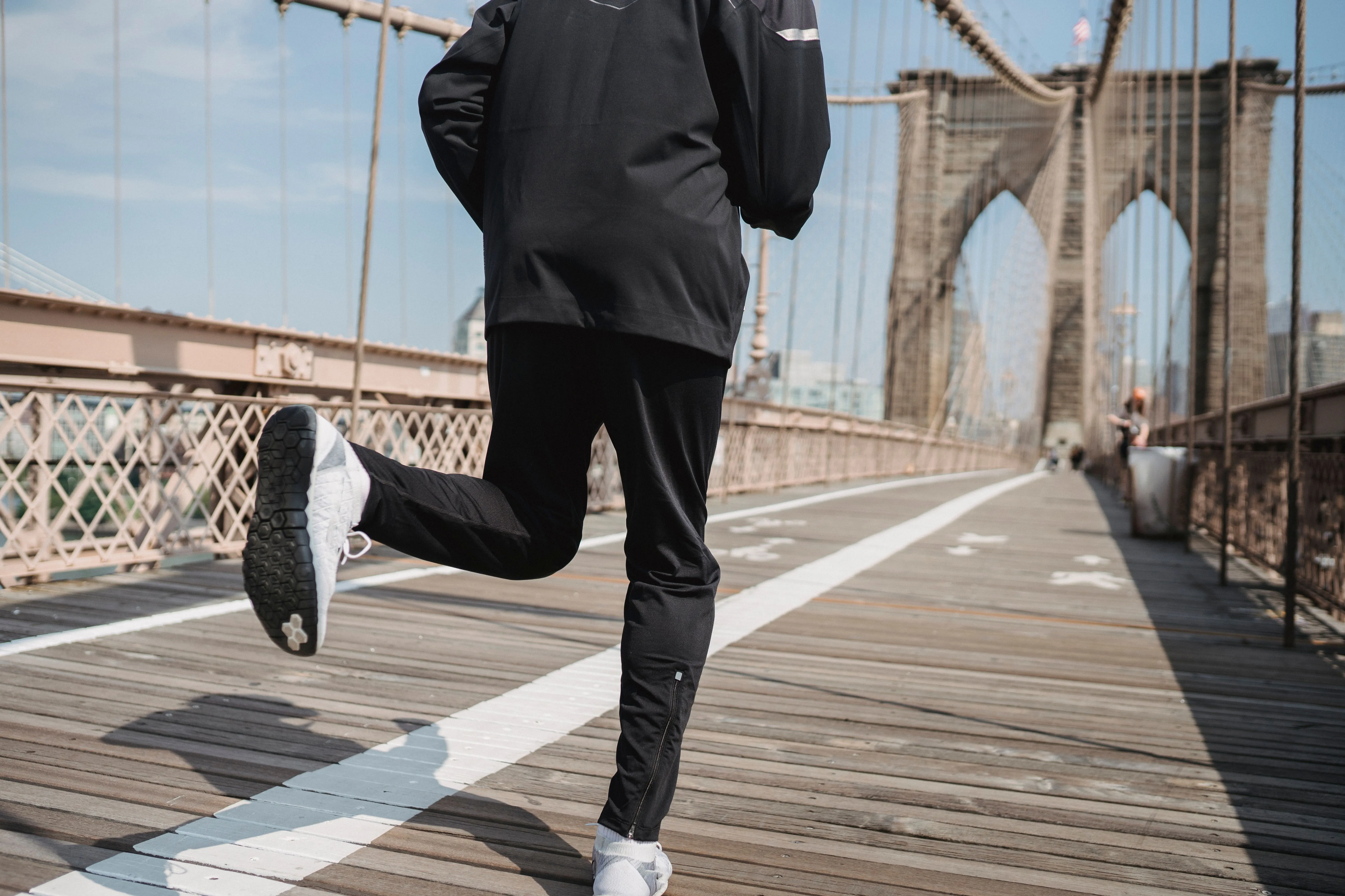 Une personne en tenue de sport court sur un pont en bois, vue de dos, avec ses chaussures au premier plan.